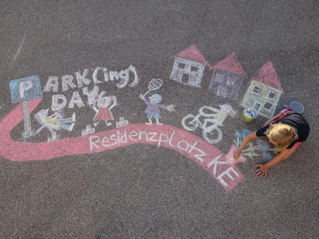 Parking Day - Kind malt mit bunter Kreide auf dem Asphalt