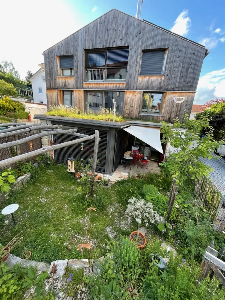 Blick auf Haus mit Garten, Rankgerüst und Wintergarten mit Dachbegrünung