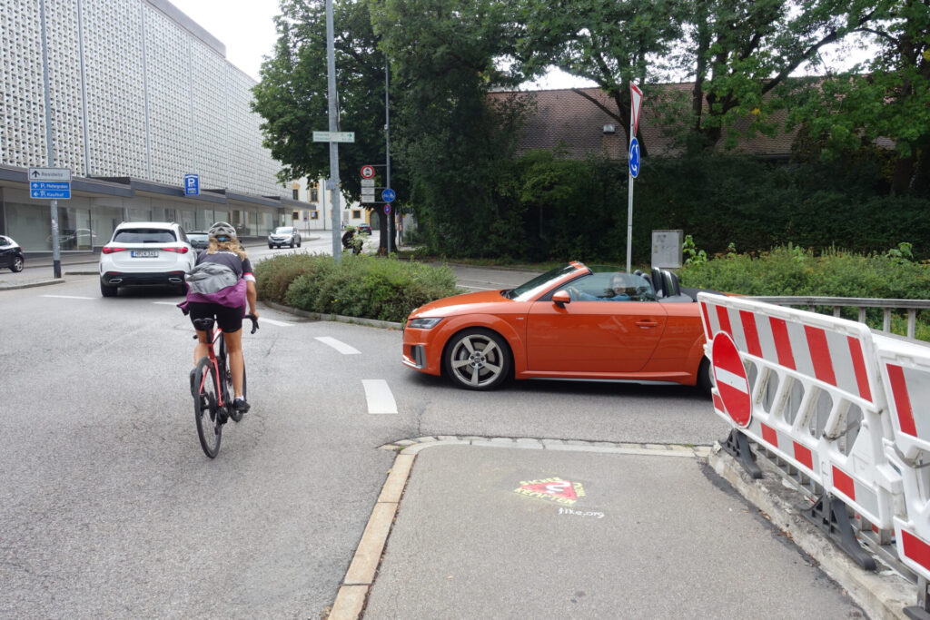 Gehweg mit Graffito "Sicher mobil in Kempten?", Auto fährt in Kreisverkehr ein