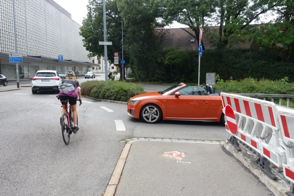 Gehweg mit Graffito "Sicher mobil in Kempten?", Auto fährt in Kreisverkehr ein
