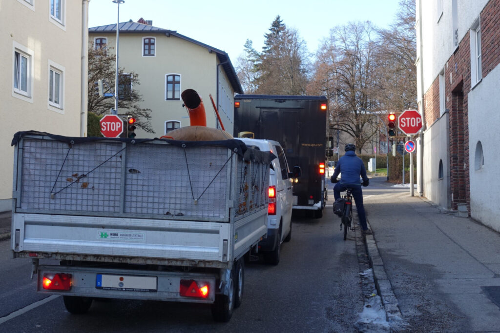 Radfahrer wartet an Ampel, eingeklemmt zwischen Bürgersteig und Autos
