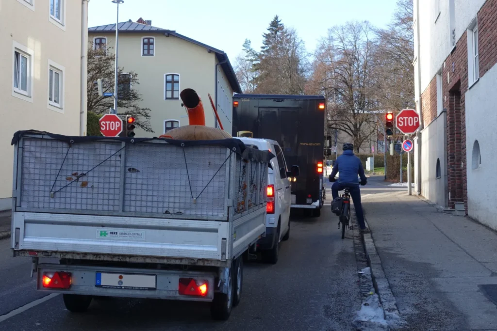 Radfahrer wartet an Ampel, eingeklemmt zwischen Bürgersteig und Autos