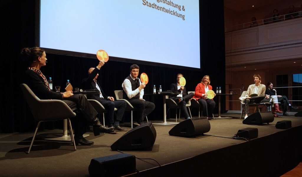 Podiumsdiskussion "OB-Kandidierende befragt", Moderatorin mit Podiumsgästen, die rote oder grüne Schilder hochhalten